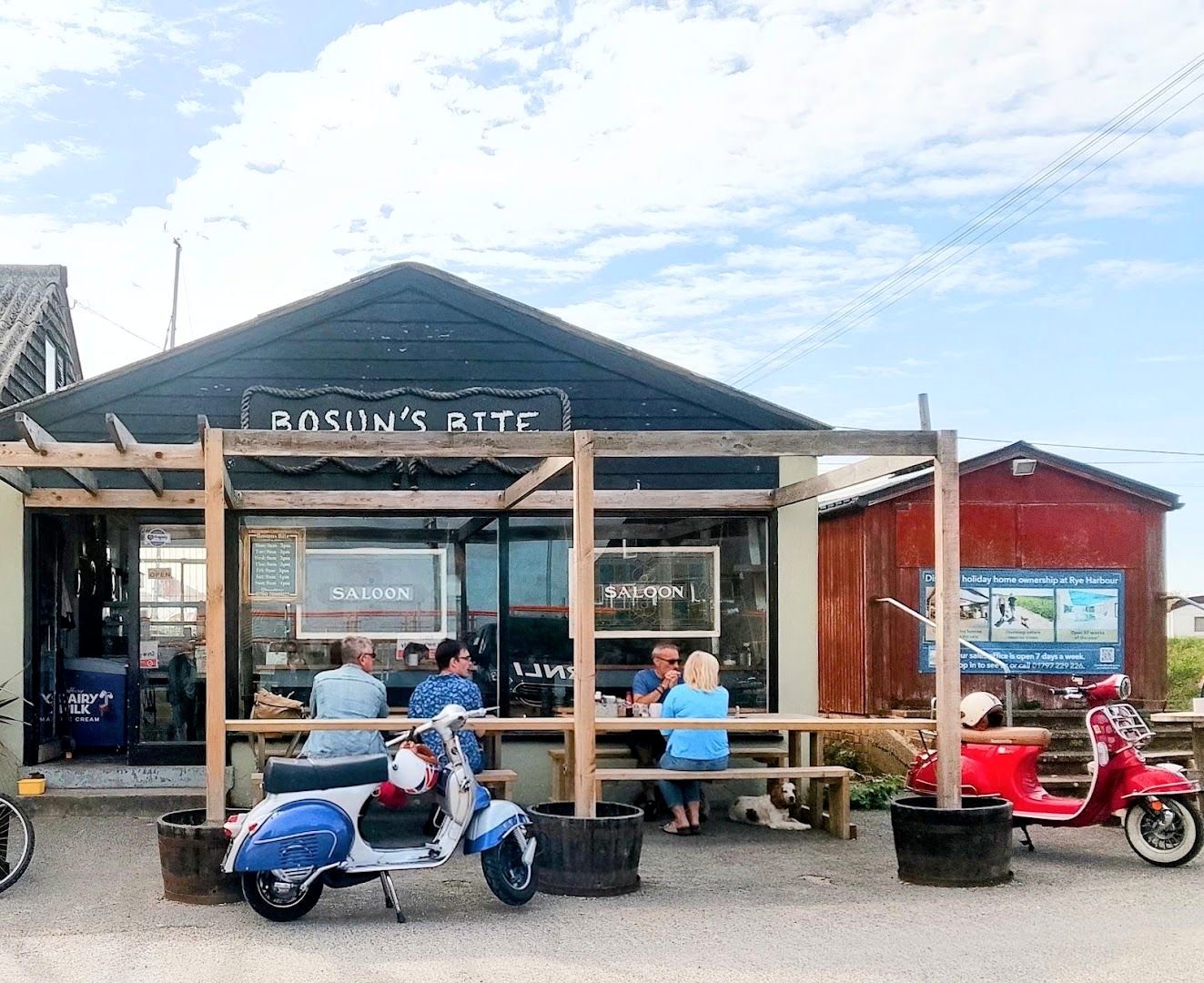 Bosun’s Bite: a black timber building with a pergola and orange shade sails, people at tables outside and two scooters parked in front