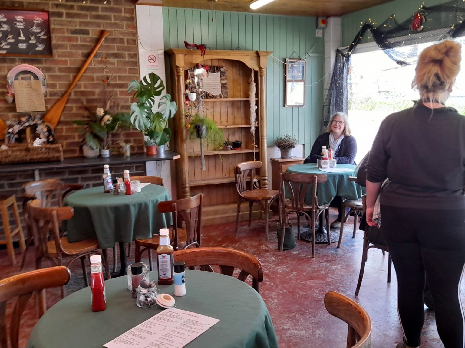 Inside: green tablecloths on round tables, wooden chairs, a wooden dresser and a boat oar on the brick wall